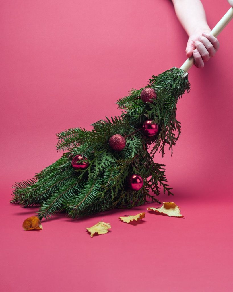 Person sweeping up leaves with a broom made to look like a Christmas tree